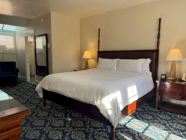 A neatly made hotel bedroom with a large bed, two lamps, and an open doorway/window area.
