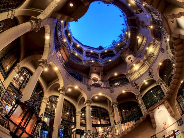 A vaulted indoor atrium with curved balconies and arches, lit by warm lights and a blue circular open sky above.