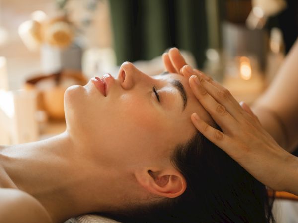 A person receiving a relaxing facial massage, with hands gently pressing the face and forehead in a spa setting.