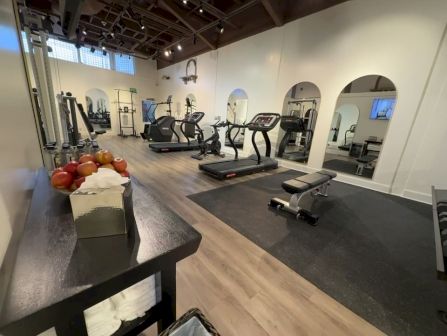 A bright gym with treadmills and cardio machines, plus a counter holding oranges by the entrance.