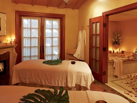 A cozy, candlelit bedroom with two beds, white bedding, wooden doors, and tropical leaves spread across the tables.