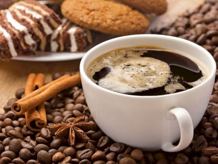 A steaming cup of coffee with cinnamon sticks and star anise, surrounded by roasted coffee beans.
