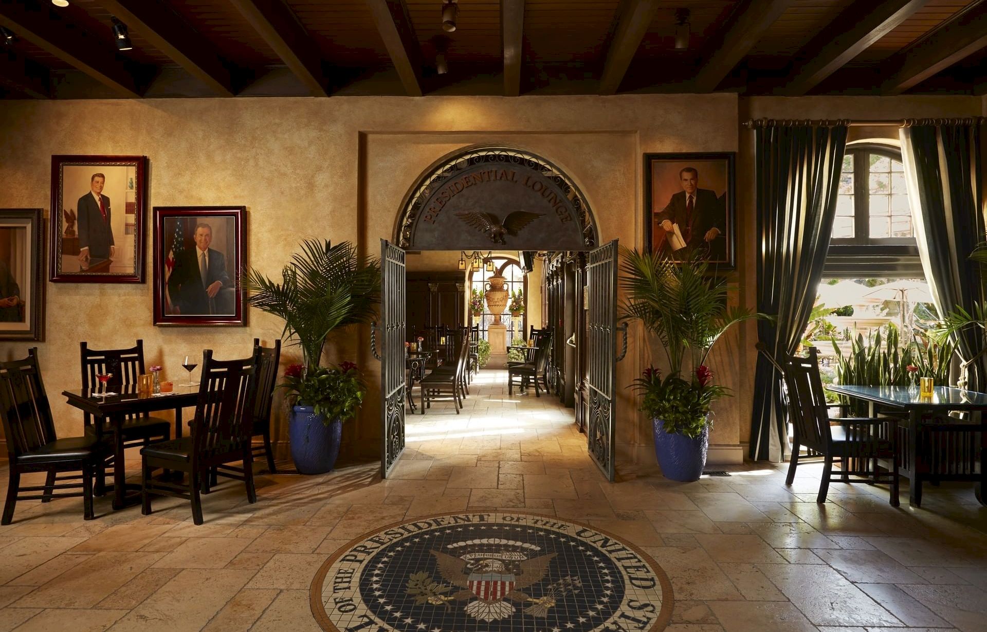 An elegant indoor lounge hallway with &ldquo;Presidential Lounge&rdquo; arch, framed portraits, plants, tables, and chairs, lit by warm ceiling lights.