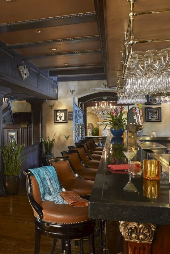 A stylish bar interior with dark wood, framed photos, a crystal chandelier, and wine glasses and bottles on the counter.