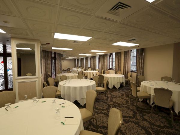 An elegant banquet hall set with round tables, white linens, and chairs, plus decorative ceiling lights and drapes.