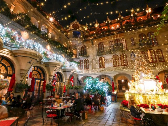 Festive courtyard at night, packed with Christmas string lights, flags, glowing decorations, and a sleigh-and-reindeer display.