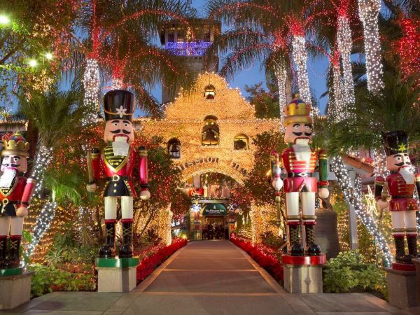 A festive Christmas light tunnel with tall nutcracker statues flanking the path, surrounded by sparkling red, gold, and white d&eacute;cor.