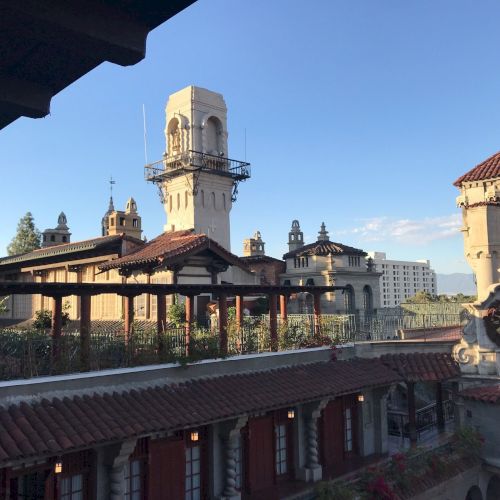 A Spanish-style courtyard with terracotta roofs, white bell towers, and arches under a clear blue sky.