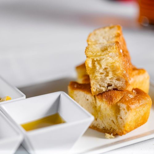 Golden toasted bread slices stacked on a white platter, with a small dab of butter beside them, ready to eat.