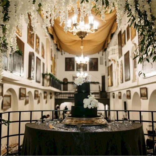 A decorated wedding reception in a courtyard with hanging lights, greenery, and a tiered cake on a table.