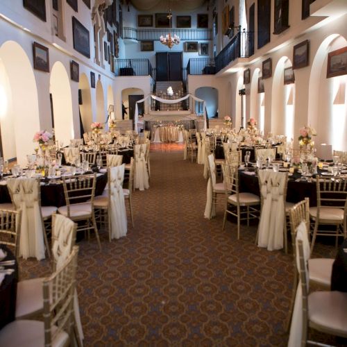An elegant banquet hall set for a wedding or event, with long tables, chairs, floral centerpieces, and candles.