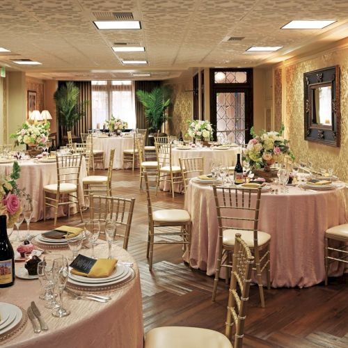 A decorated banquet hall with round tables, candles, flowers, and golden chairs arranged for a formal event.