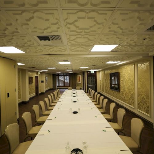 A formal meeting room with a long white table, neatly set place cards, beige chairs, and ornate ceiling and wall molding.