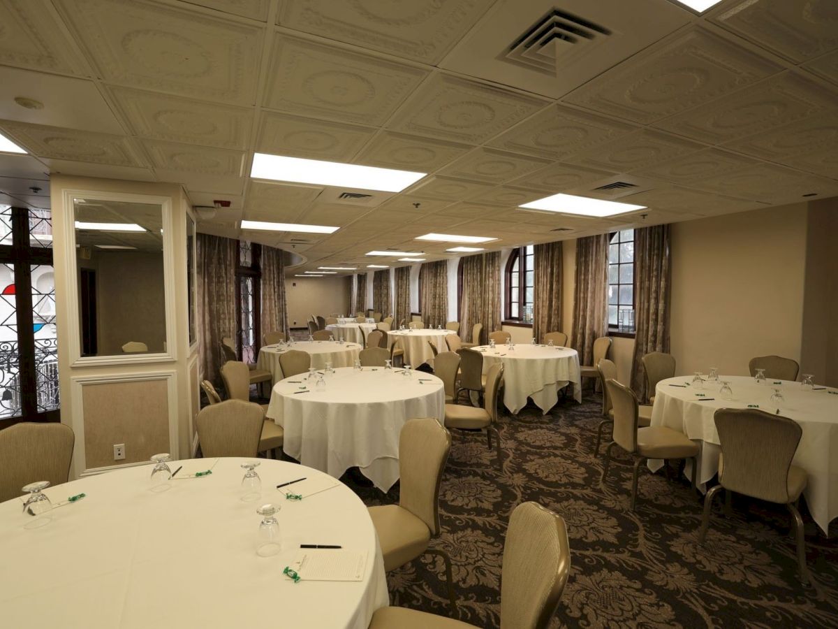 An elegant banquet meeting room with round tables set for dining, upholstered chairs, and long curtains along large windows.
