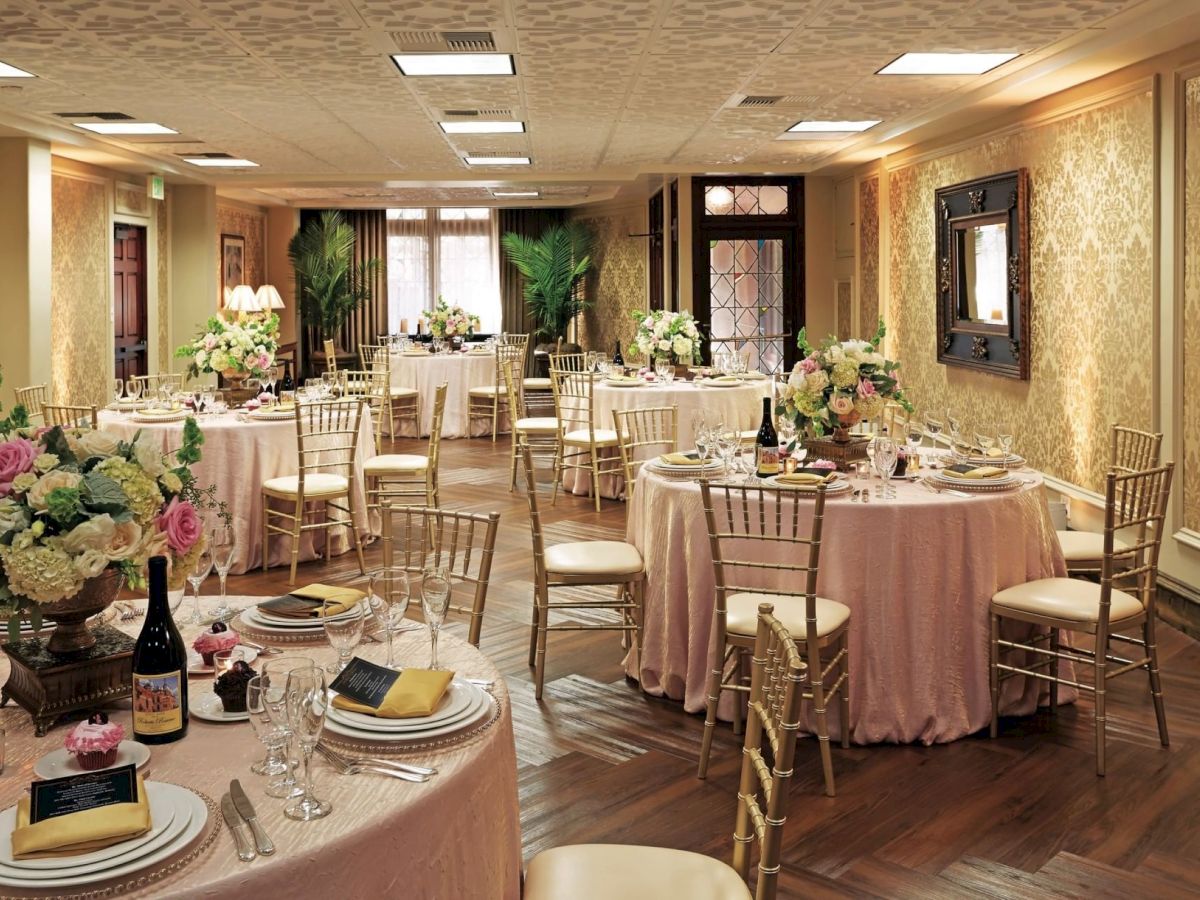 A formal banquet hall setup with round tables, gold chairs, candles, and large floral centerpieces.