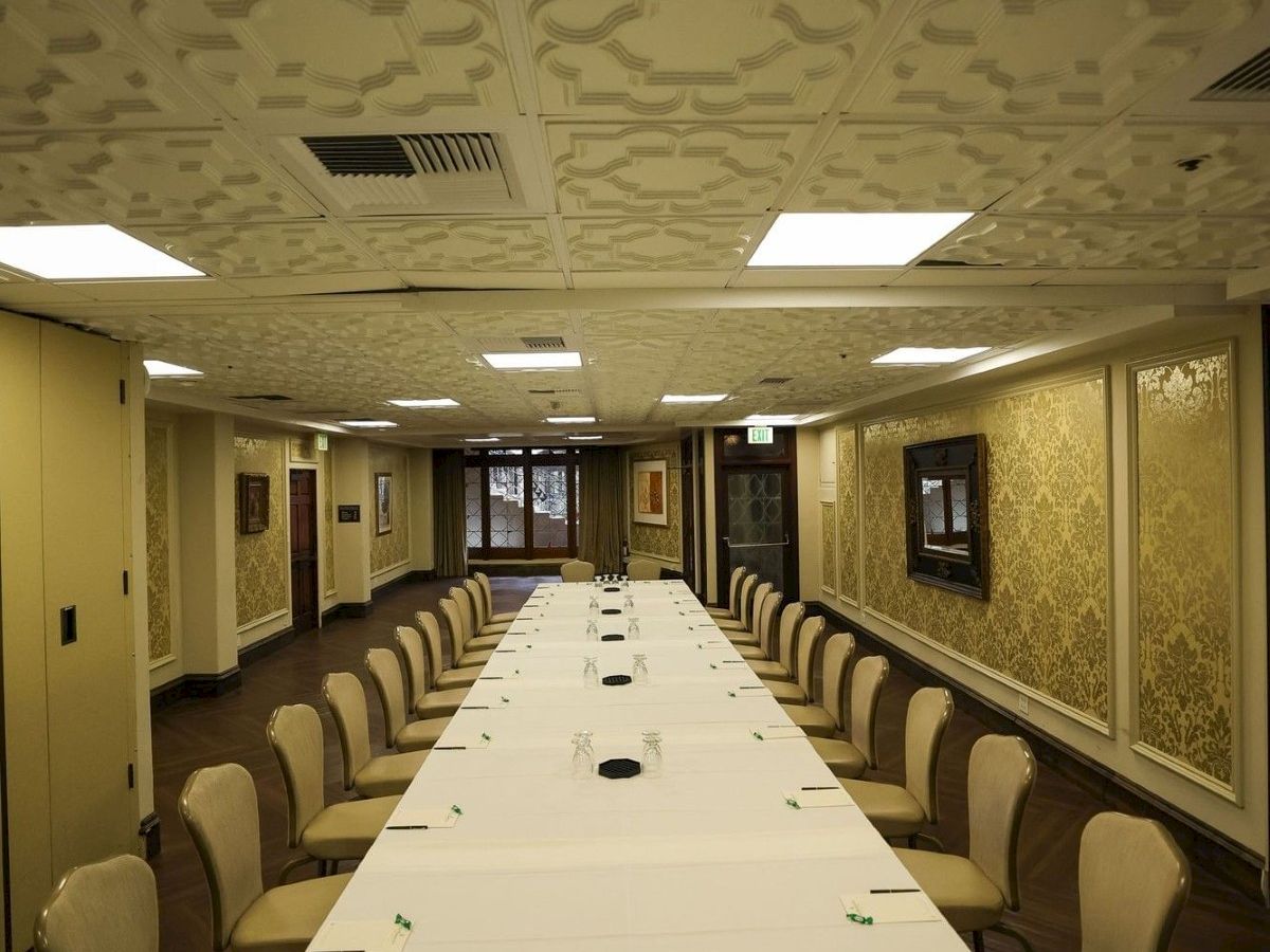 A formal meeting room with a long white table, many chairs, and ornate coffered ceiling and decorative walls.