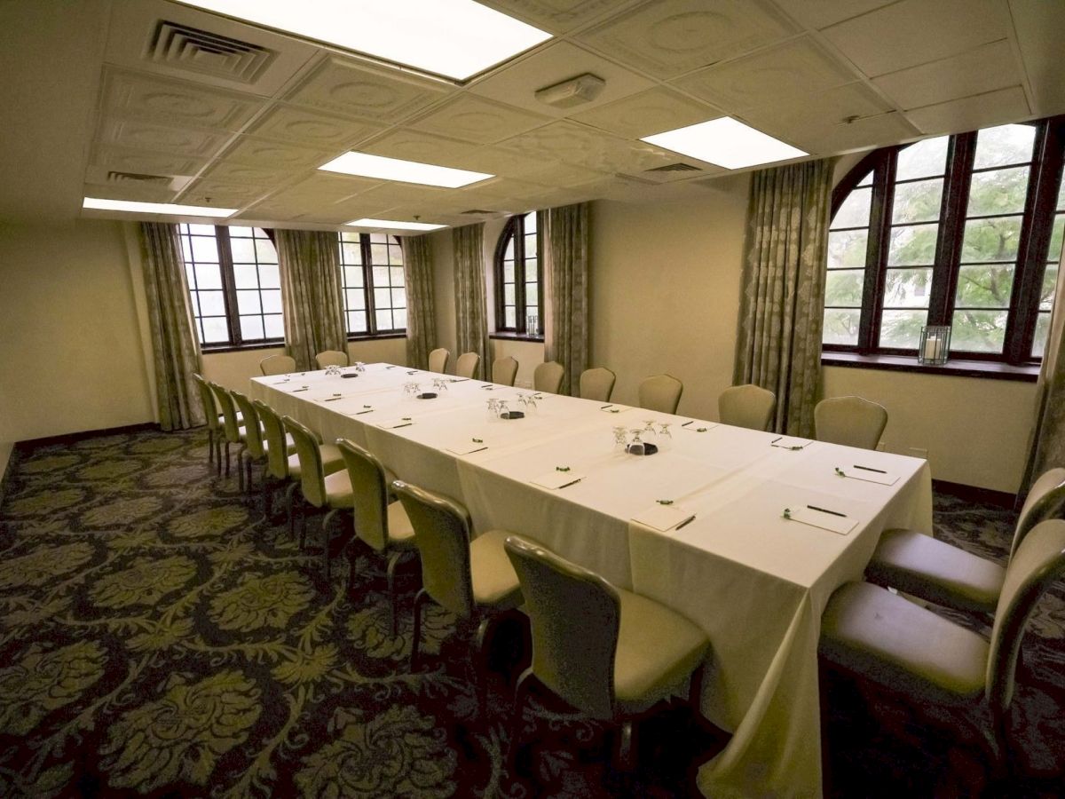 A set dining room for a formal meeting, with a long white table set with place settings, green chairs, and large arched windows.