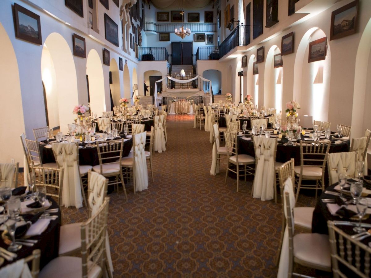 An elegant banquet hall set for a wedding, with tables, chairs, candlelight, and floral centerpieces along a grand aisle.