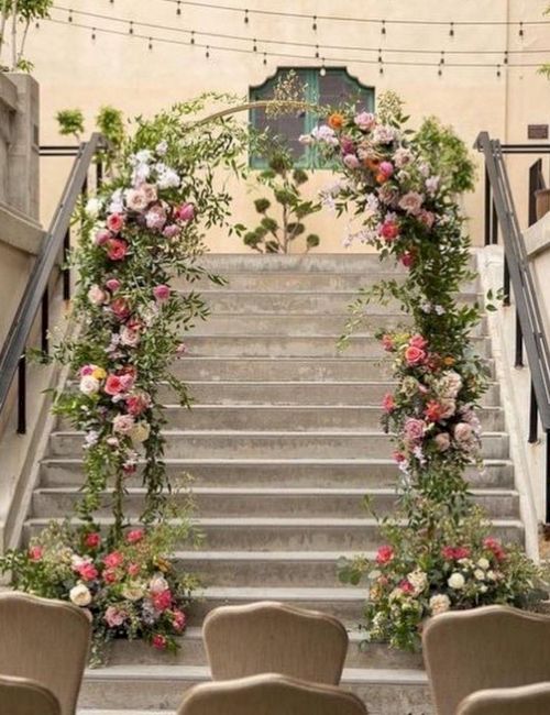 A grand staircase is dressed with lush greenery and colorful flowers, framed by hanging lights above and seating at the bottom.