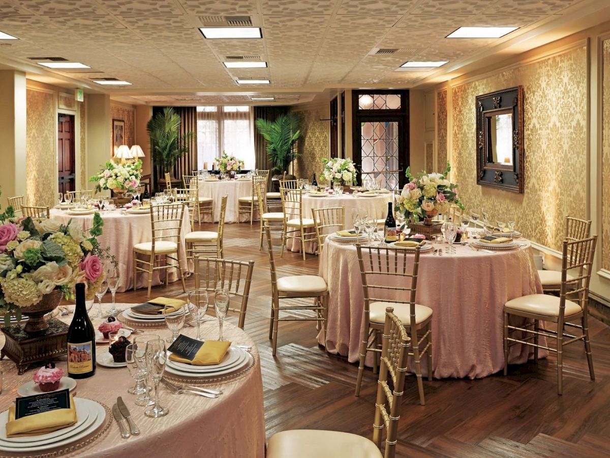 A ballroom set for a wedding or banquet with round tables, gold chairs, candles, glassware, and floral centerpieces.