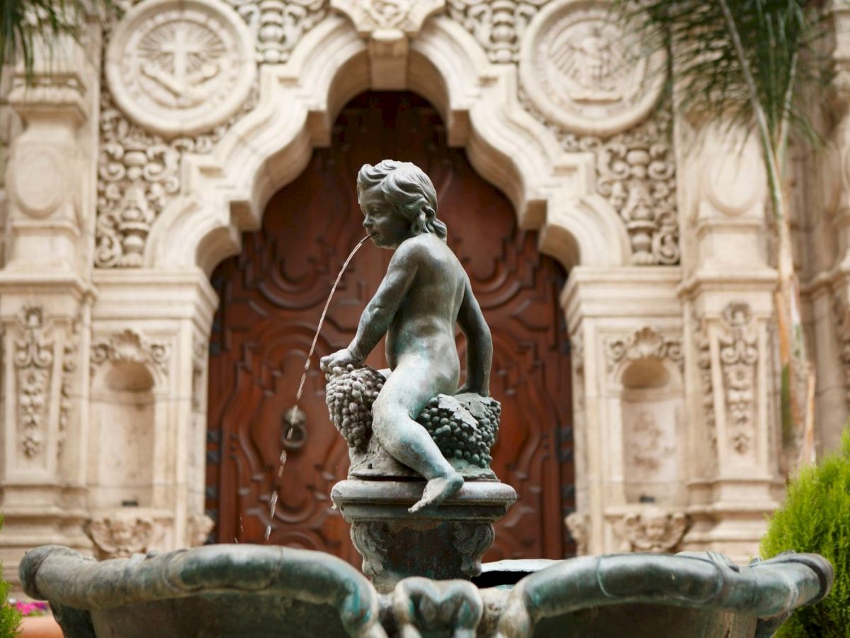 A bronze fountain statue of a woman pouring water into a basin, set before an ornate stone building with carved arches.
