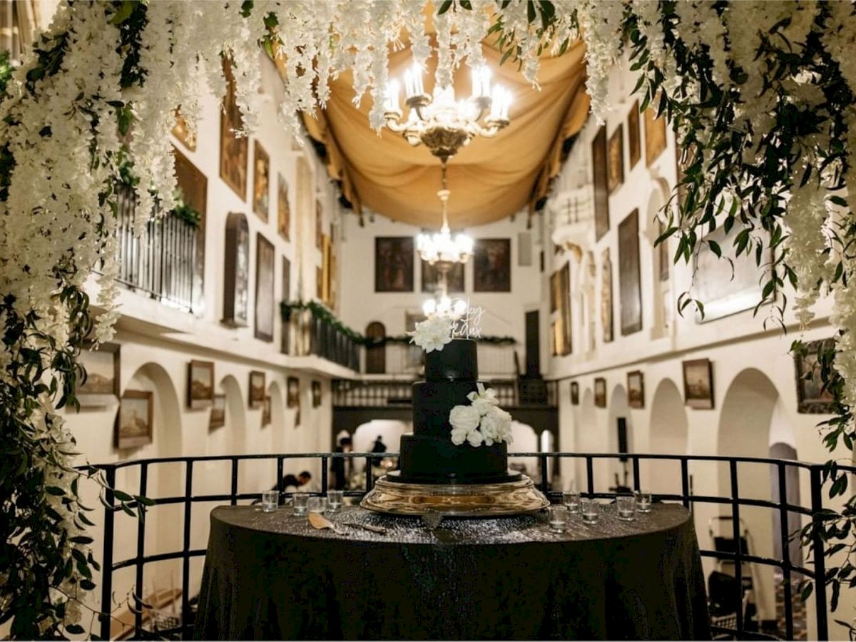 A decorated wedding ceremony space with hanging lights, greenery, and a cake table in an ornate hall.