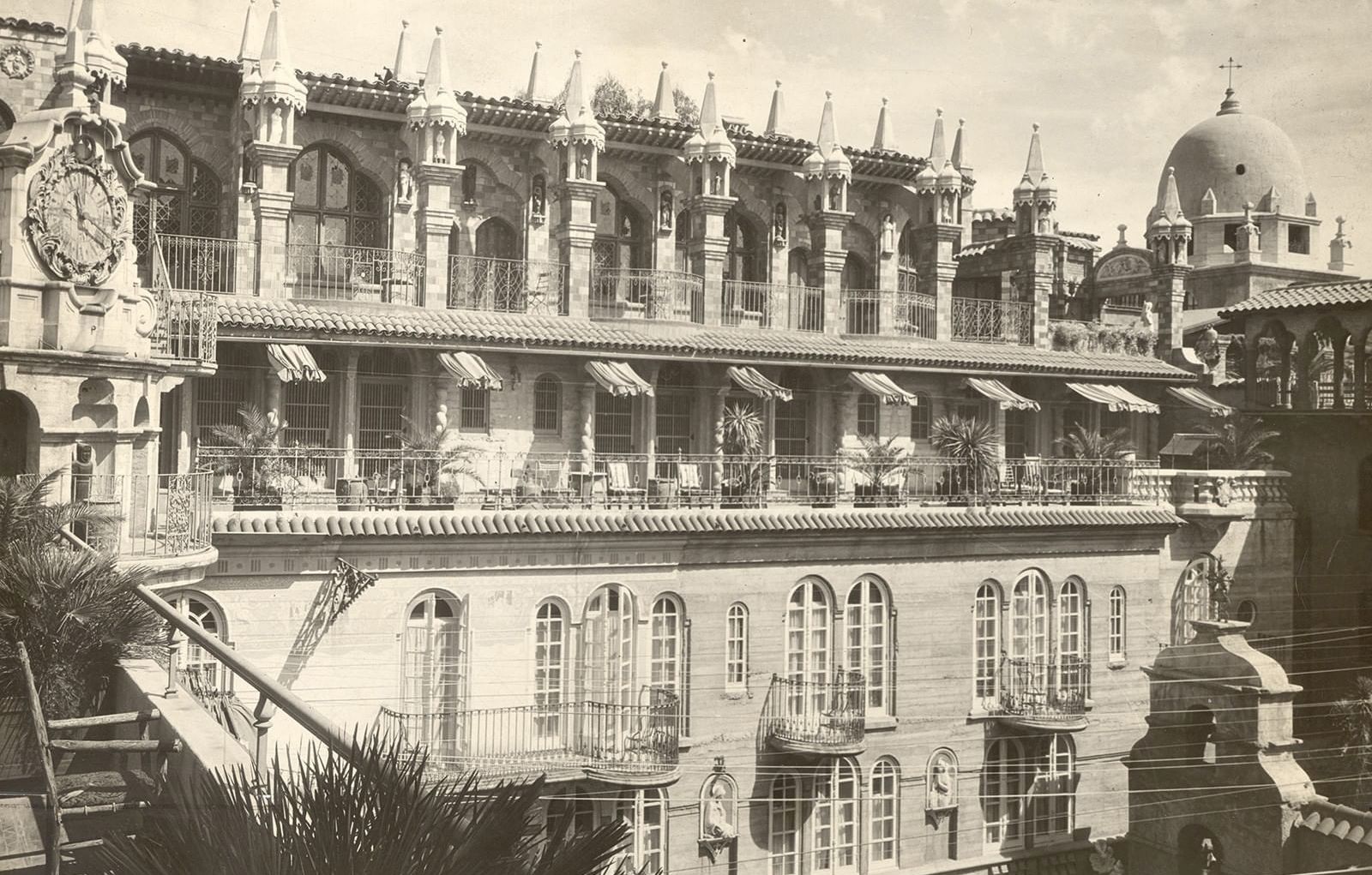 An old grand palace building with arched colonnades, ornate towers, domes, and a rooftop terrace, captured in a vintage photo.
