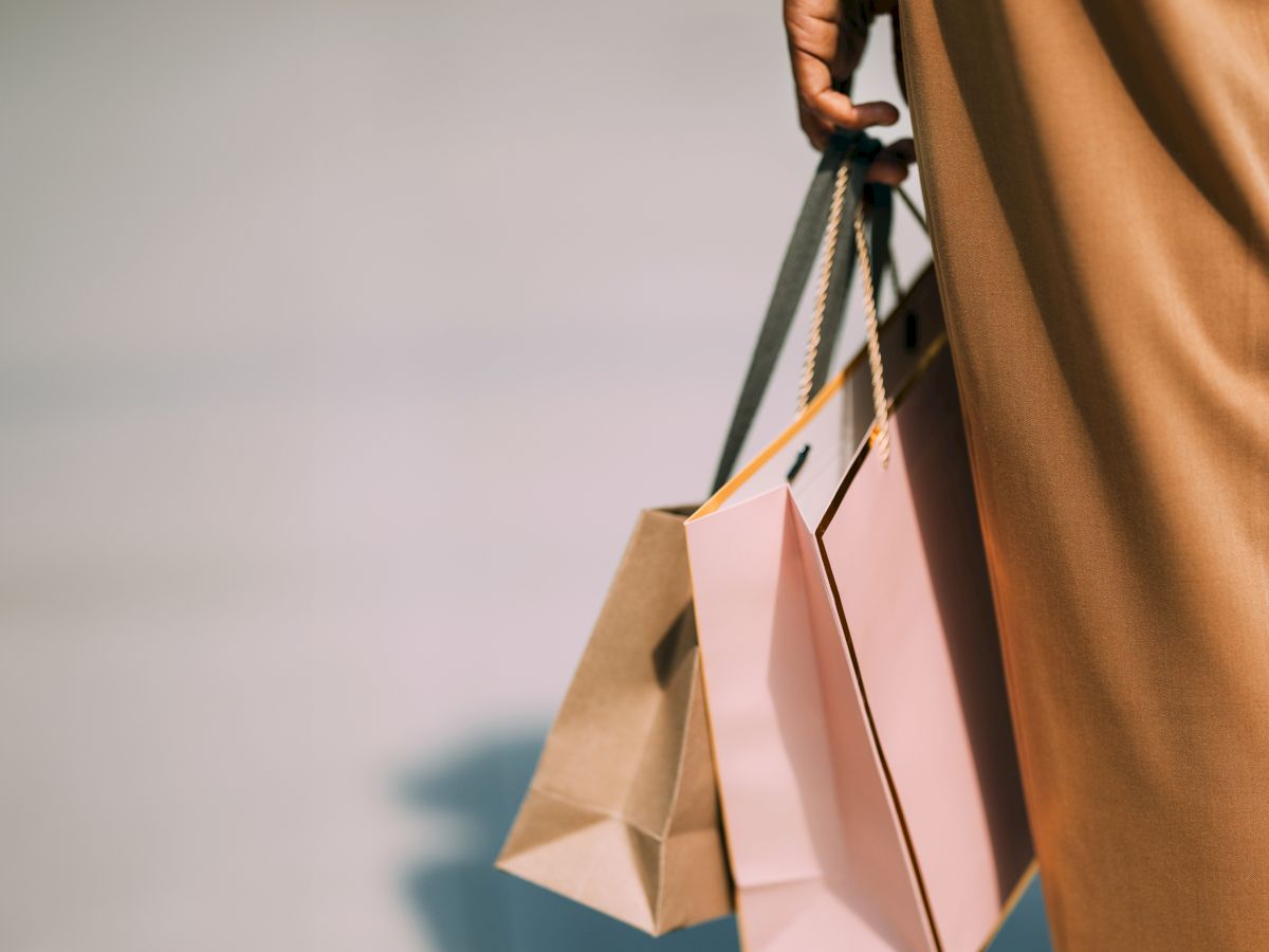 Close-up of a person holding shopping bags, with their arm and a small microphone-like accessory in view.