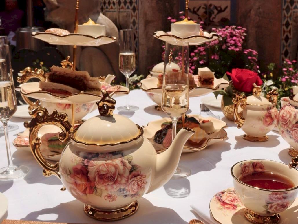 An ornate afternoon tea set with a floral teapot, gold accents, and cups on a decorated table.