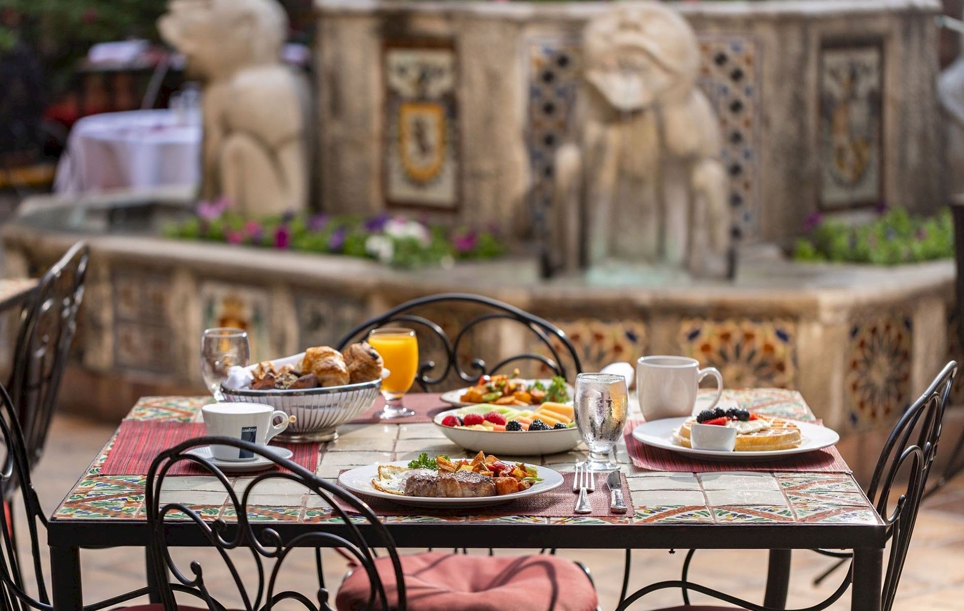 Outdoor patio table set with breakfast&mdash;plates, croissants, fruit, juice, and coffee&mdash;sitting in front of a decorative stone wall.